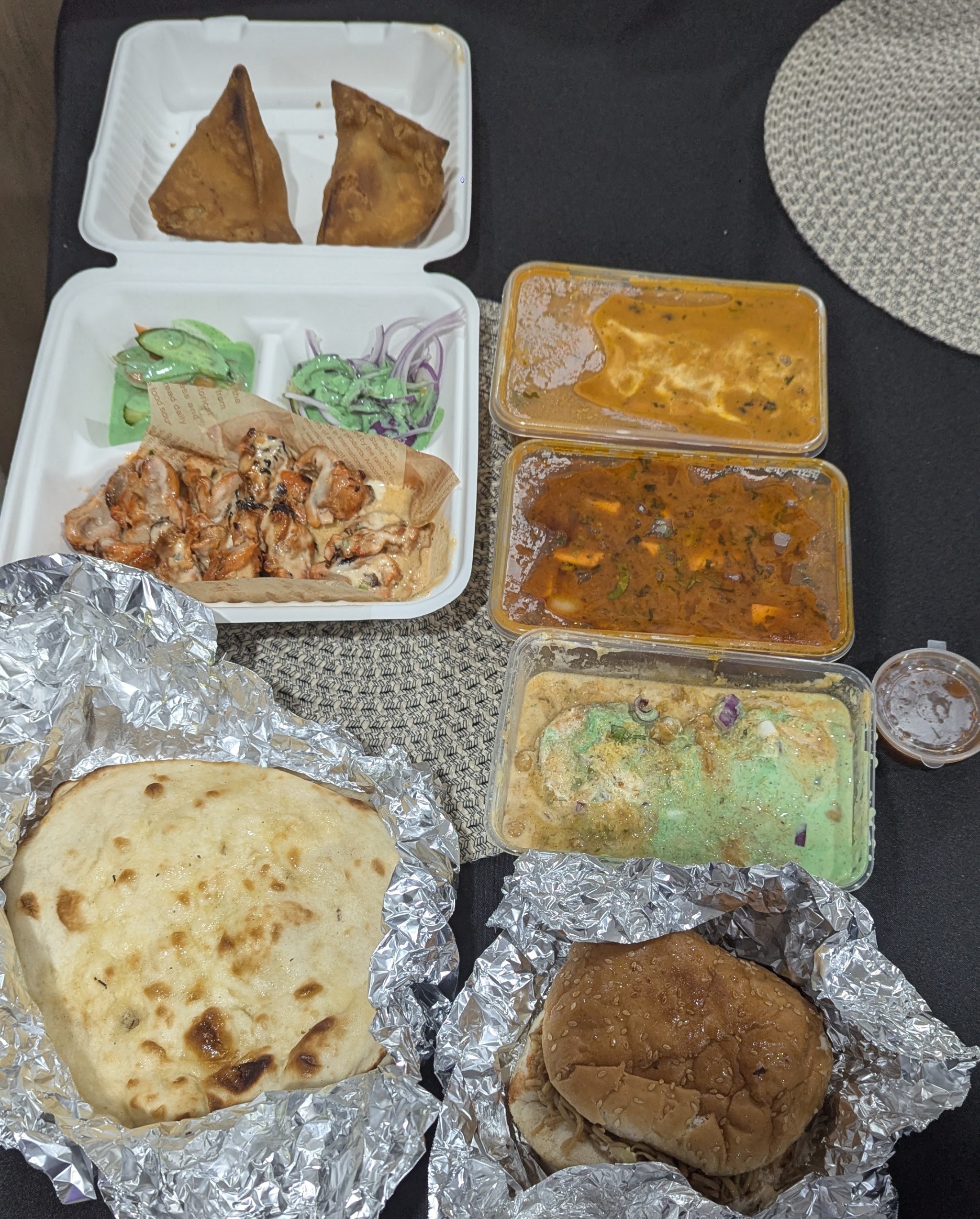 A Tandoor Bros takeaway spread: samosas, tandoori chicken, three curries, naan and kulcha